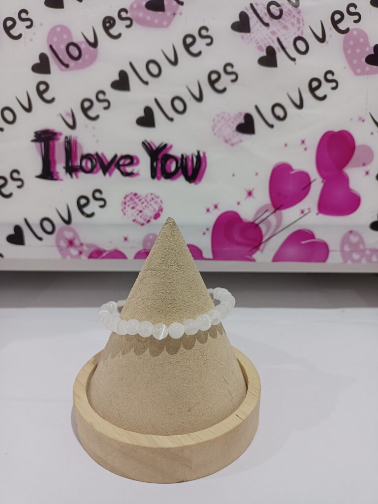 Pulsera de cuentas blancas sobre un soporte de madera con fondo de corazones rosados